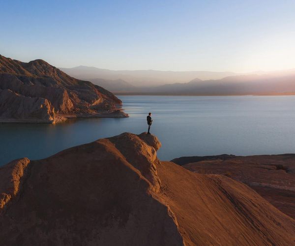 Person meditating peacefully outdoors near a calm lake at sunrise.